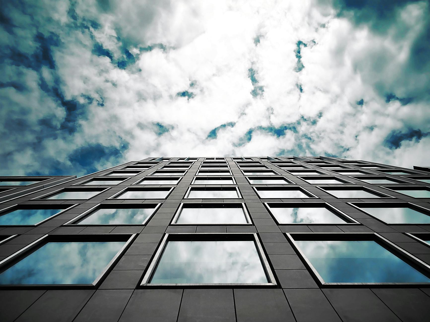 brown high rise building under sky full of white clouds